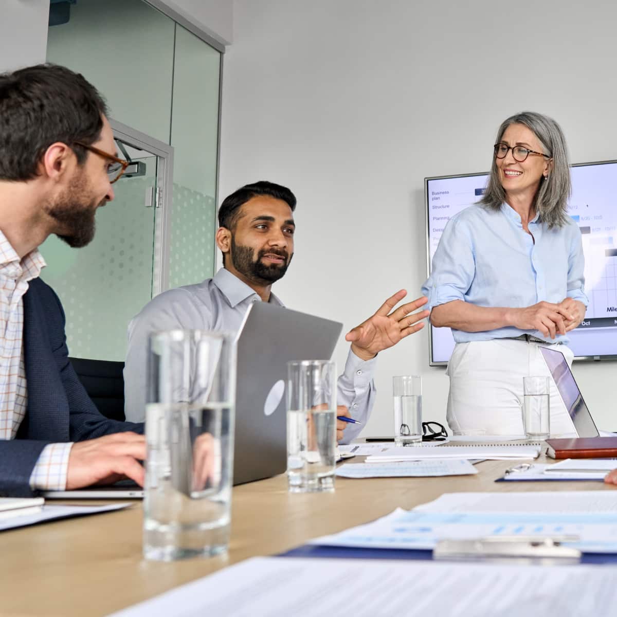 Three coworkers sitting around at a desk in conference room talking and working with one another. 