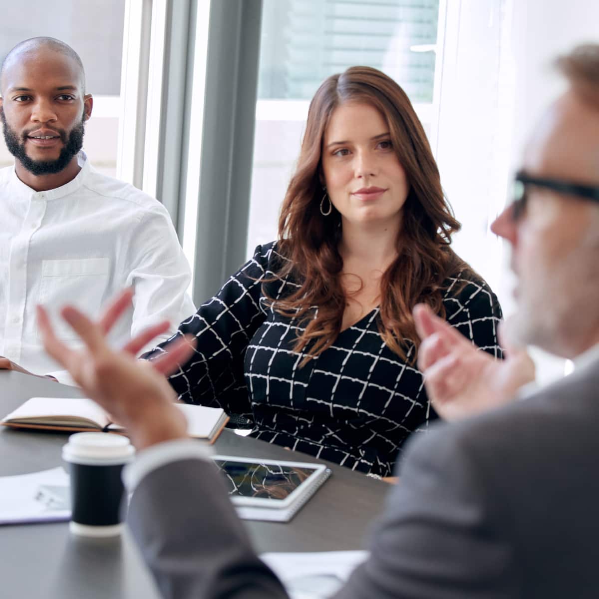 Three co workers sitting around desk in conference room working together. 