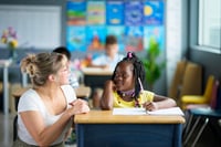 Teacher kneeling and talking with a student's at her desk