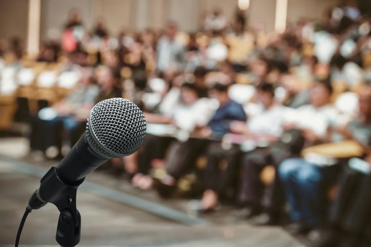 microphone over a blurred photo of a school board meeting