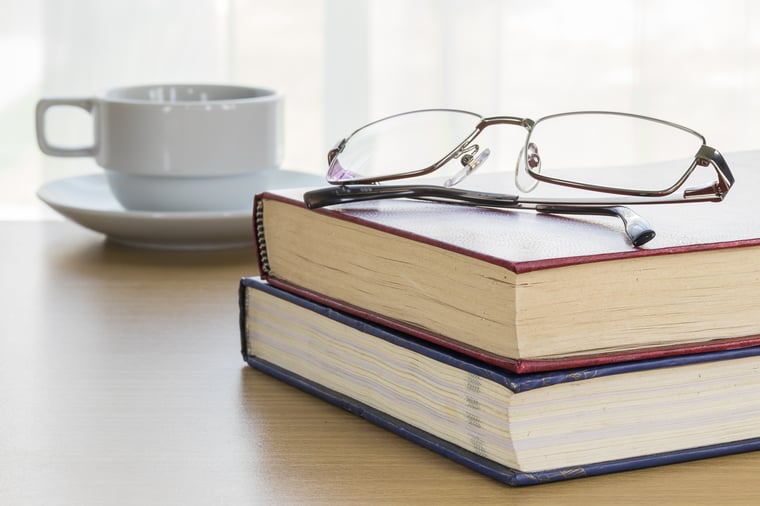 2 books with glasses on top and a cup a coffee 